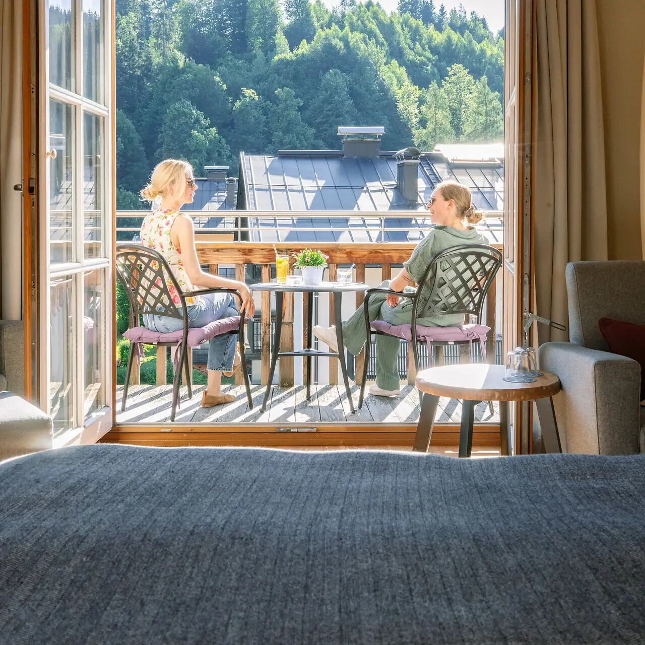 Zimmer mit Balkon Zwei Frauen sitzen auf einem Balkon und blicken aus einem Fenster.