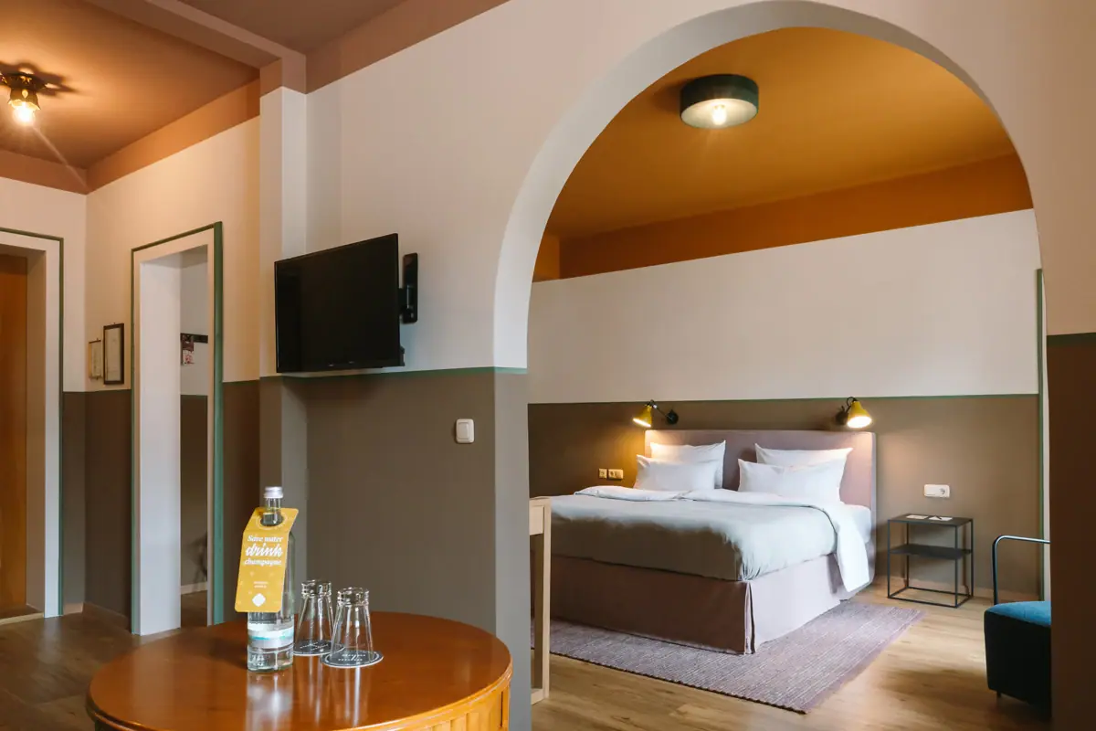 Suite im HENRI Hotel Garmisch-Partenkirchen Ein großes Hotelzimmer mit einem Durchgang vom Wohnbereich in das Schlafzimmer mit einem Bett und einem Fernseher an der Wand.