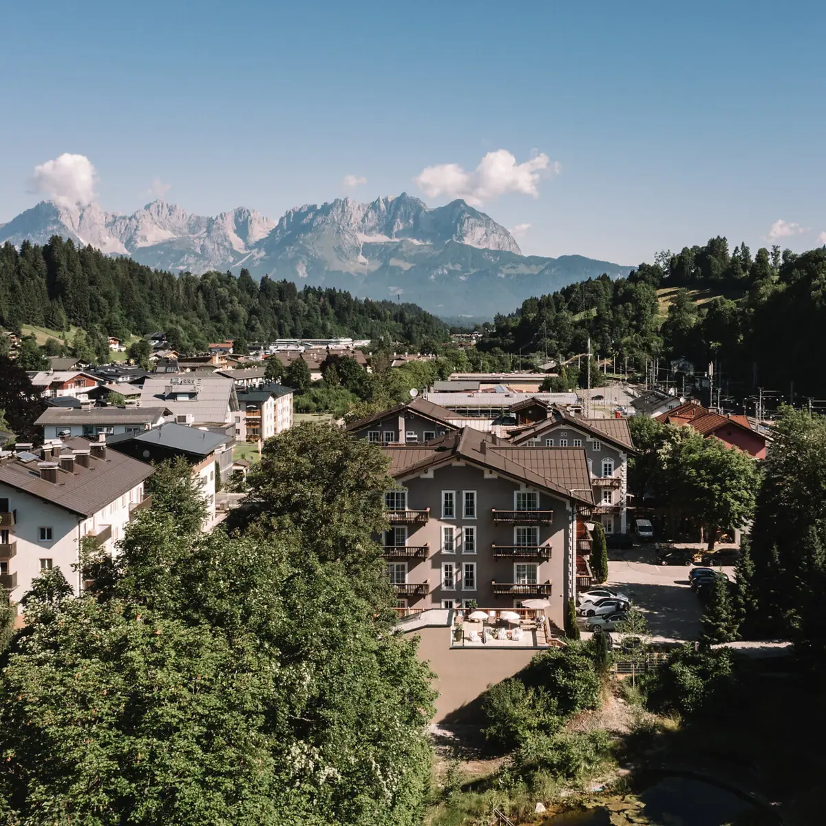 HENRI Hotel Kitzbühel vor den Alpen Kleinstadt mit Bäumen und Bergen im Hintergrund.