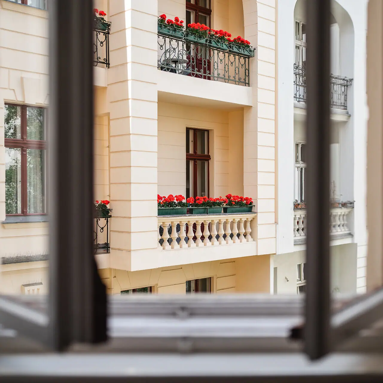 HENRI Berlin Ausblick Balkon Ein Fenster mit Blick auf ein Gebäude mit Blumen auf dem Balkon.