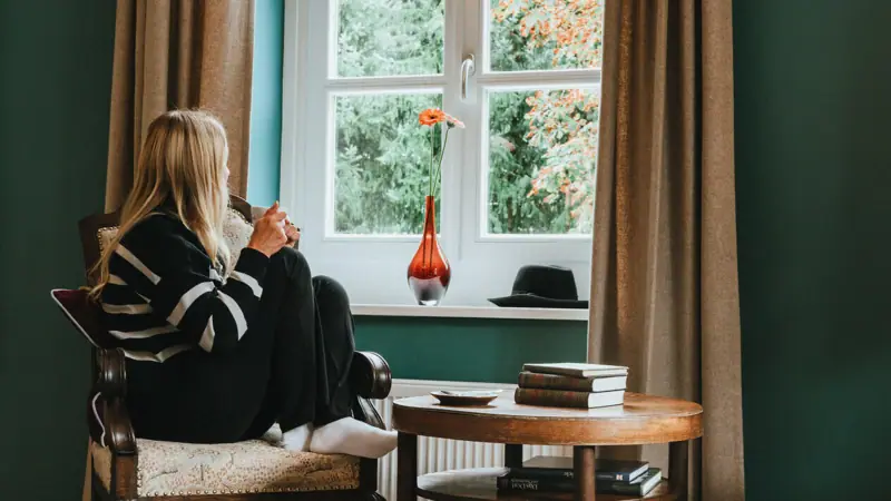 Zimmer im HENRI Kitzbühel Eine Frau sitzt auf einem Stuhl und schaut aus dem Fenster.