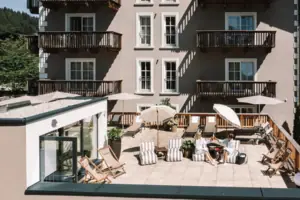 HENRI Kitzbühel SPA Terrasse Eine Gruppe von Menschen sitzt auf einer Terrasse mit Sonnenschirmen und Stühlen.