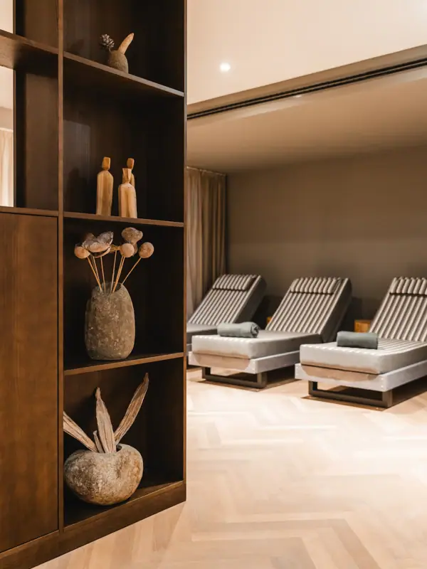 HENRI Kitzbühel Ruhebereich Ein Raum mit Stühlen und einem Regal mit Vasen und Blumen.